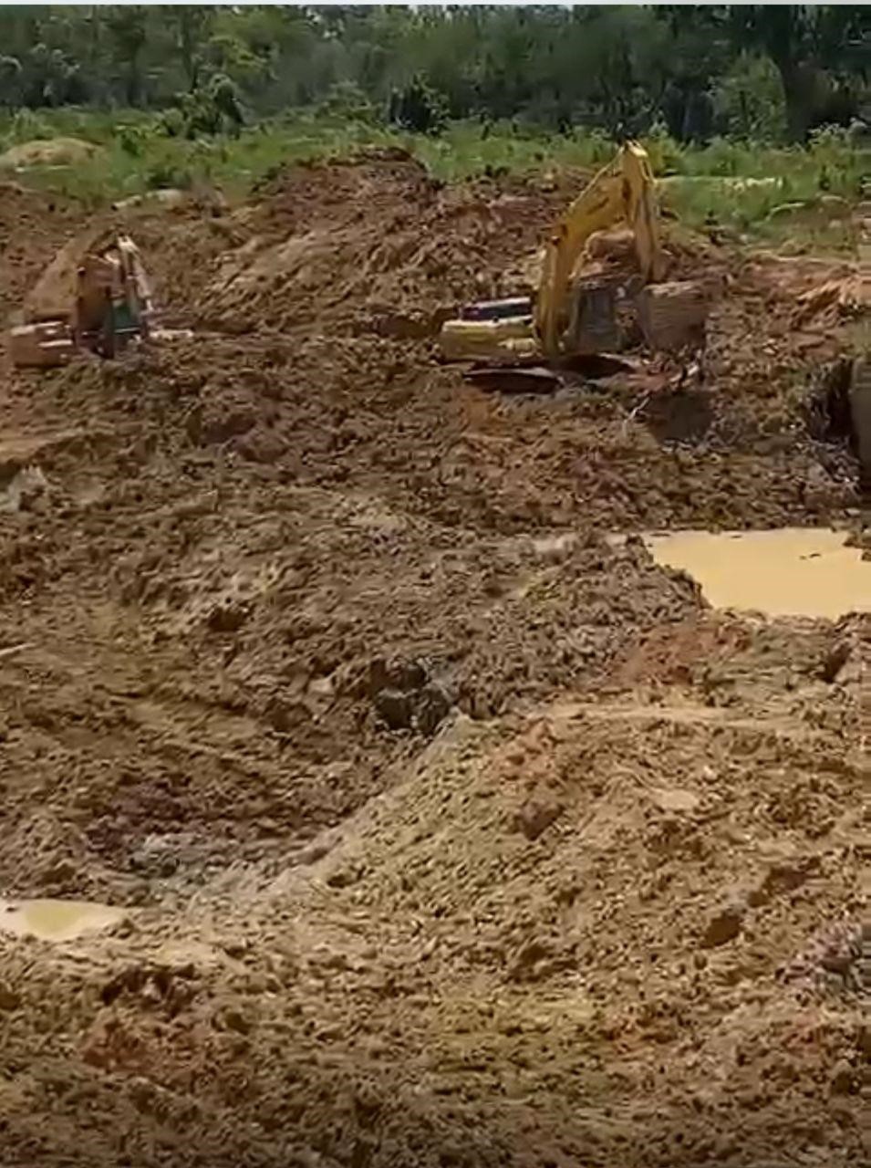 L'image montre une vaste zone de terre excavée et boueuse, typique d'une carrière clandestine d'orpaillage qui utilise des engins lourds. Cette technique détruit la structure du sol et le couvert végétal / Ph:SD