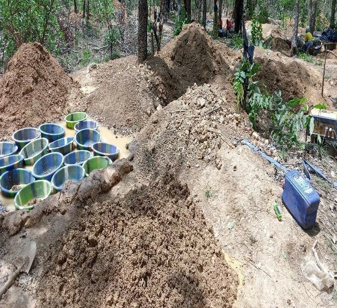 Cette photo illustre le processus de lavage du minerai pour séparer l'or. Les bassines colorées (souvent appelées "panning" ou "batées") et les grandes piles de sable et de gravier sont caractéristiques de l'orpaillage manuel ou semi-mécanisé / Ph:SD